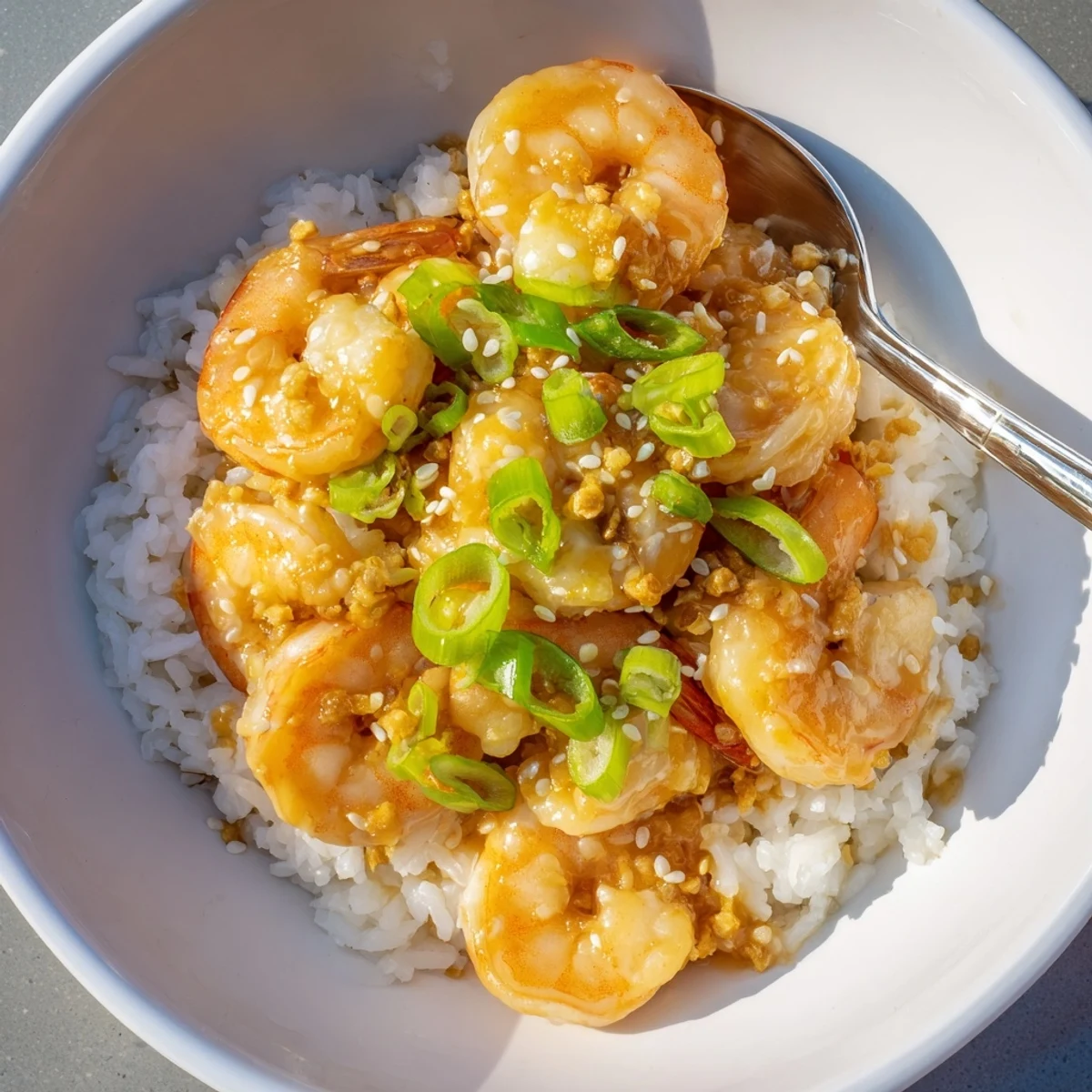 Vibrant bowl of honey garlic shrimp and rice garnished with green onions and sesame.  