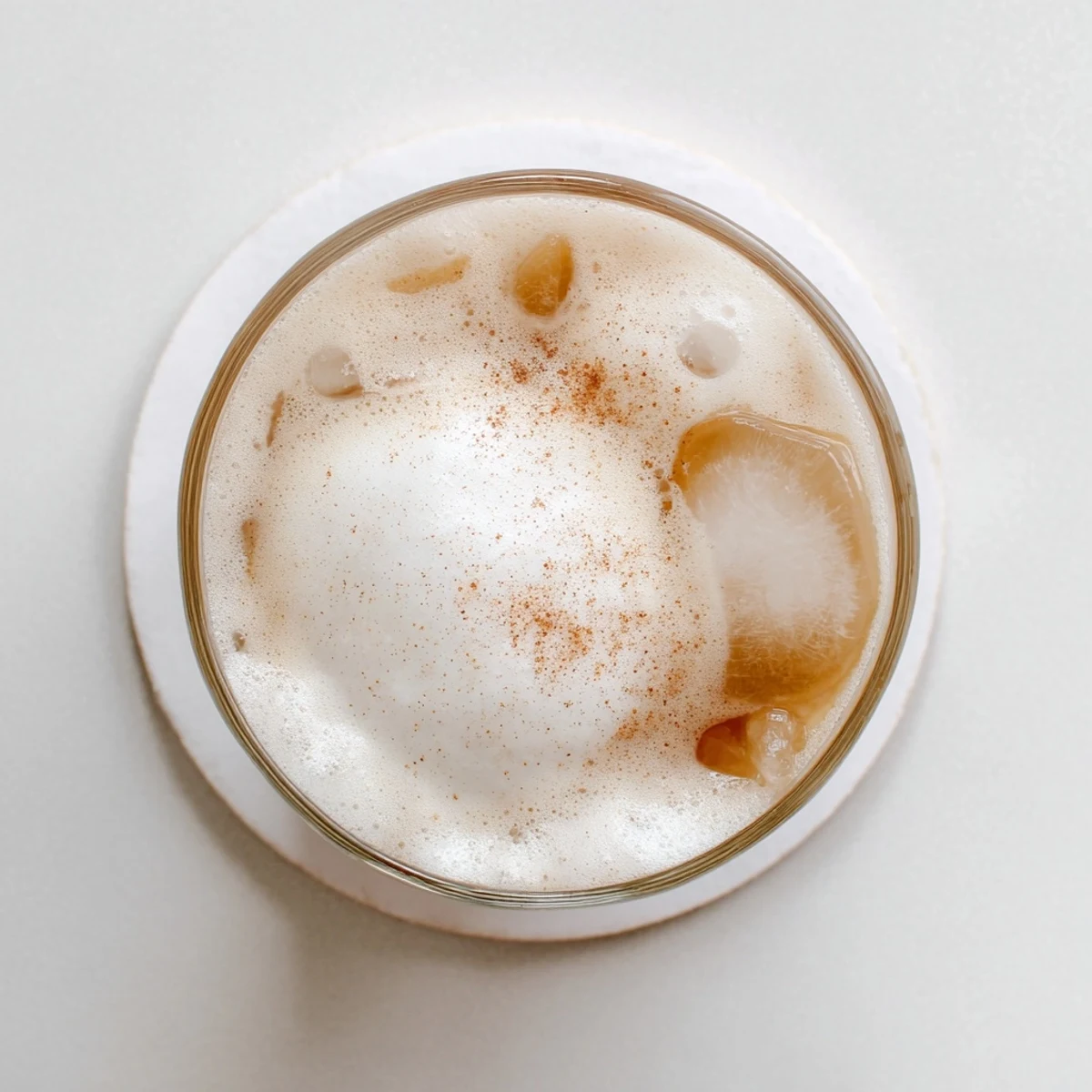 Iced chai tea layered with creamy cold foam over ice cubes, serving a refreshing beverage on a sunny day.  