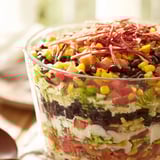 A clear glass bowl showcases the Southwest Sunset Palette, a layered salad with fresh garnishes.