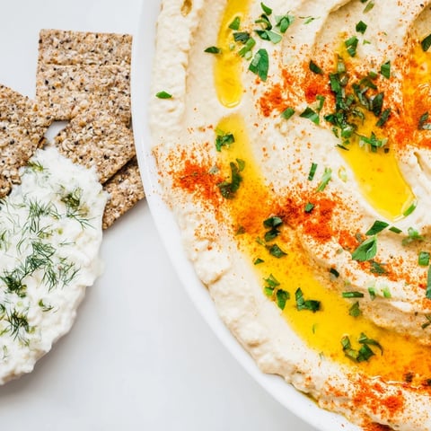 Two party-perfect dip bowls: creamy herb yogurt and classic hummus, ready to scoop with crackers.