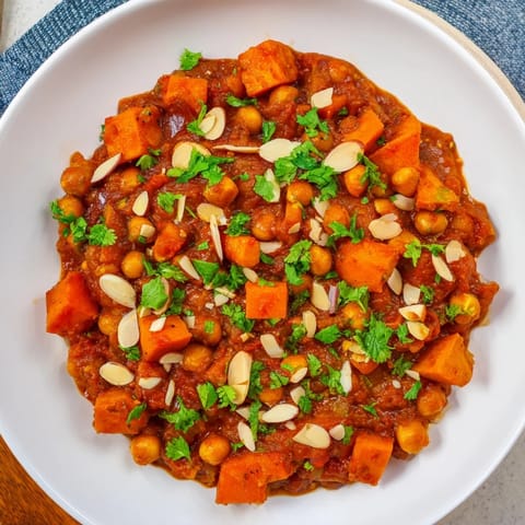 Close-up of a bubbling Moroccan Chickpea & Sweet Potato Tagine, with tender vegetables in a rich sauce.