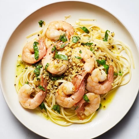 Steaming plate of lemon herb pasta with shrimp, garnished with fresh parsley and lemon wedges nearby.