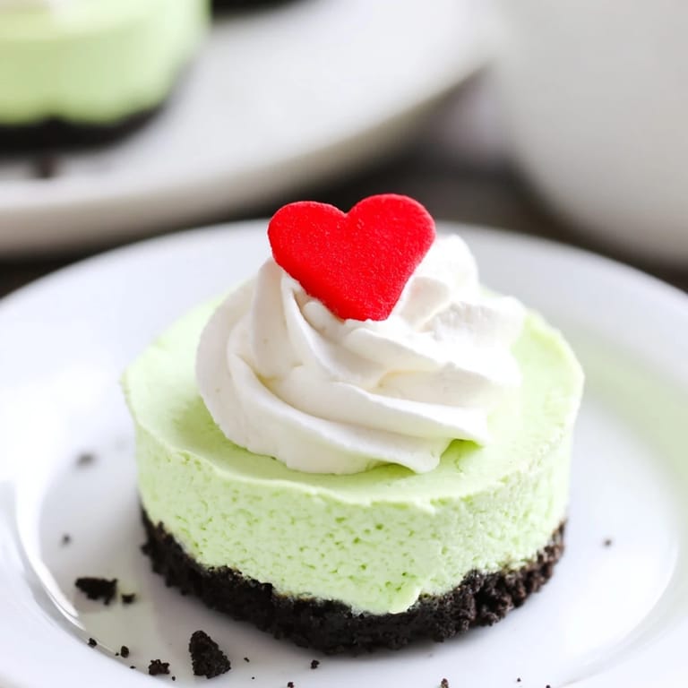 A close-up of Grinch Mini Cheesecakes shows off fluffy whipped cream and a red heart sprinkle ready to eat.