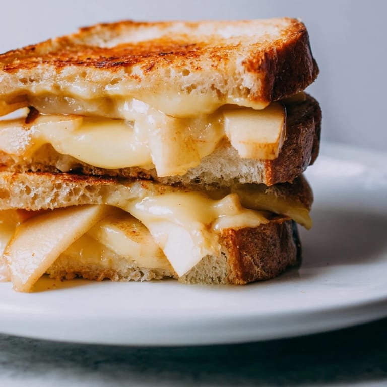 A close-up of a buttery grilled cheese with crisp apple layers and gooey smoked Gouda, sliced to reveal the interior.  