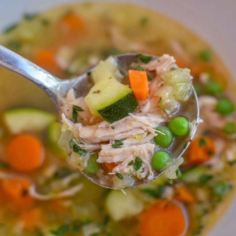 Bright Spring Garden Chicken Soup served with a lemon wedge and crusty bread, perfect for a light, healthy meal.