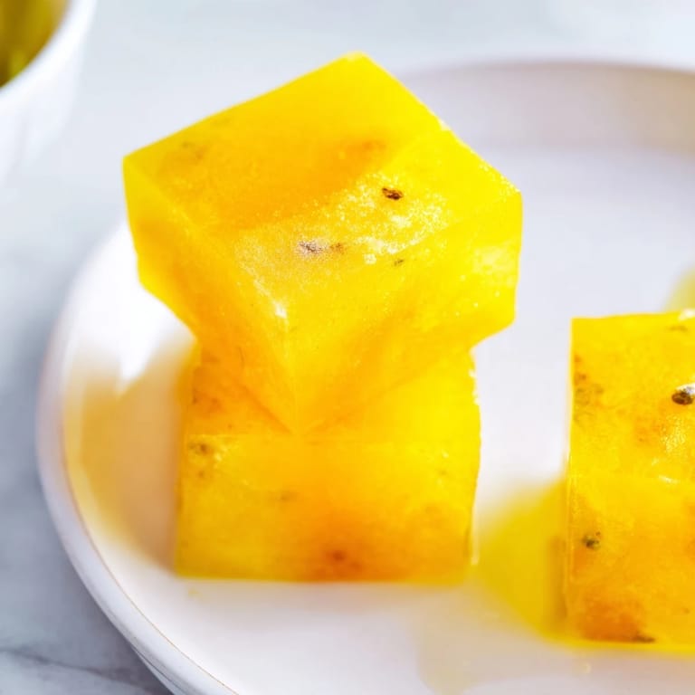 A close-up shows the vibrant orange hue of these Lemon Ginger Turmeric Wellness Cubes in a freezer tray, highlighting their smooth texture and healthful ingredients.